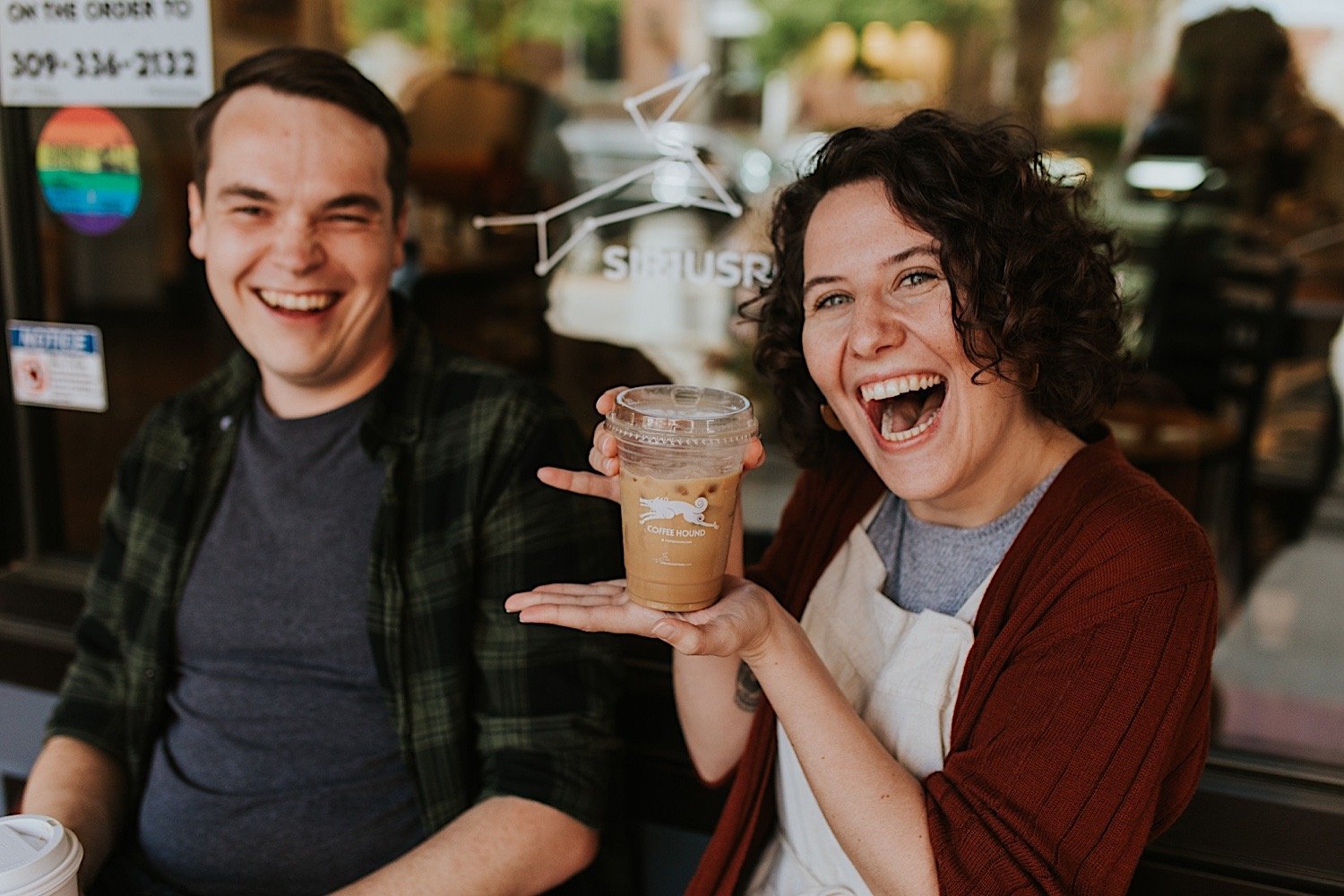 Engaged couple sits with an iced coffee outside of the coffee hound during their engagement session