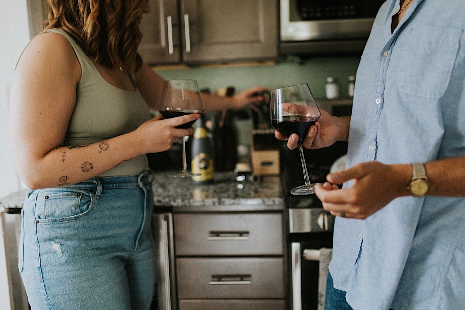 An image of a married couple holding glasses of wine in their kitchen.  The image just shows their torsos and arms during their in home session