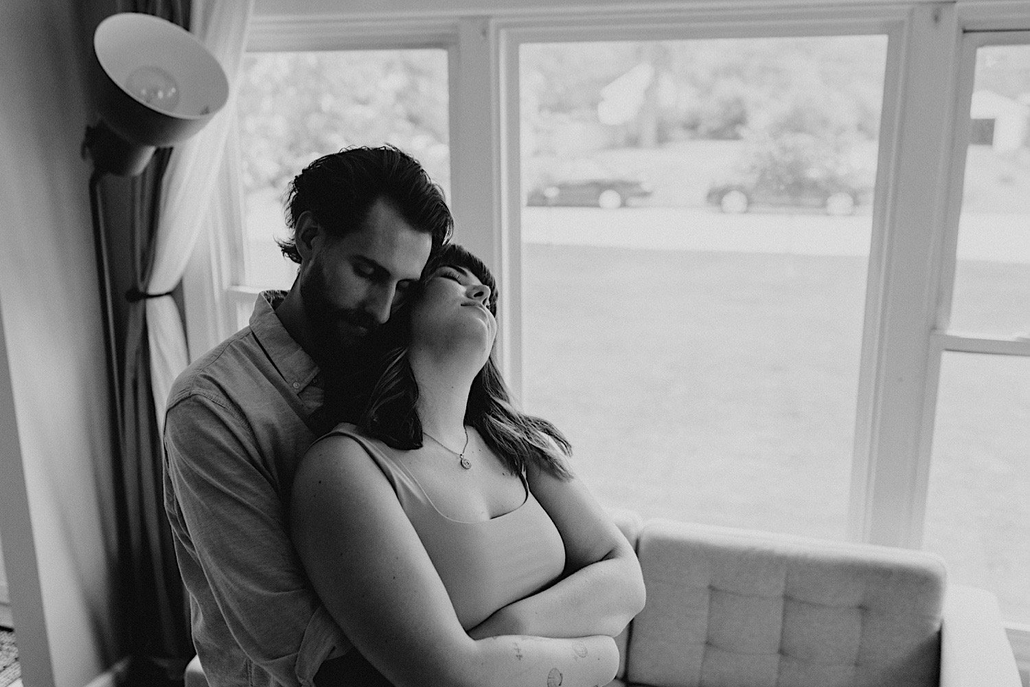 A couple stands in front of their window embracing and breathing together during their in-home session in the Chicago suburbs.
