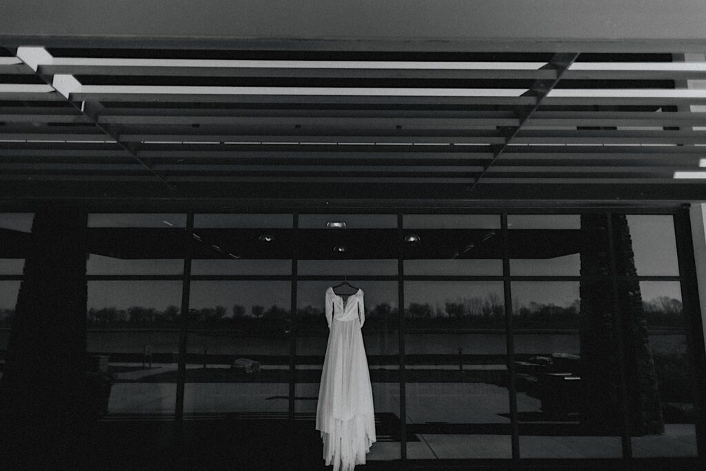 Black and white photo of a wedding dress hanging in front of a wall of windows