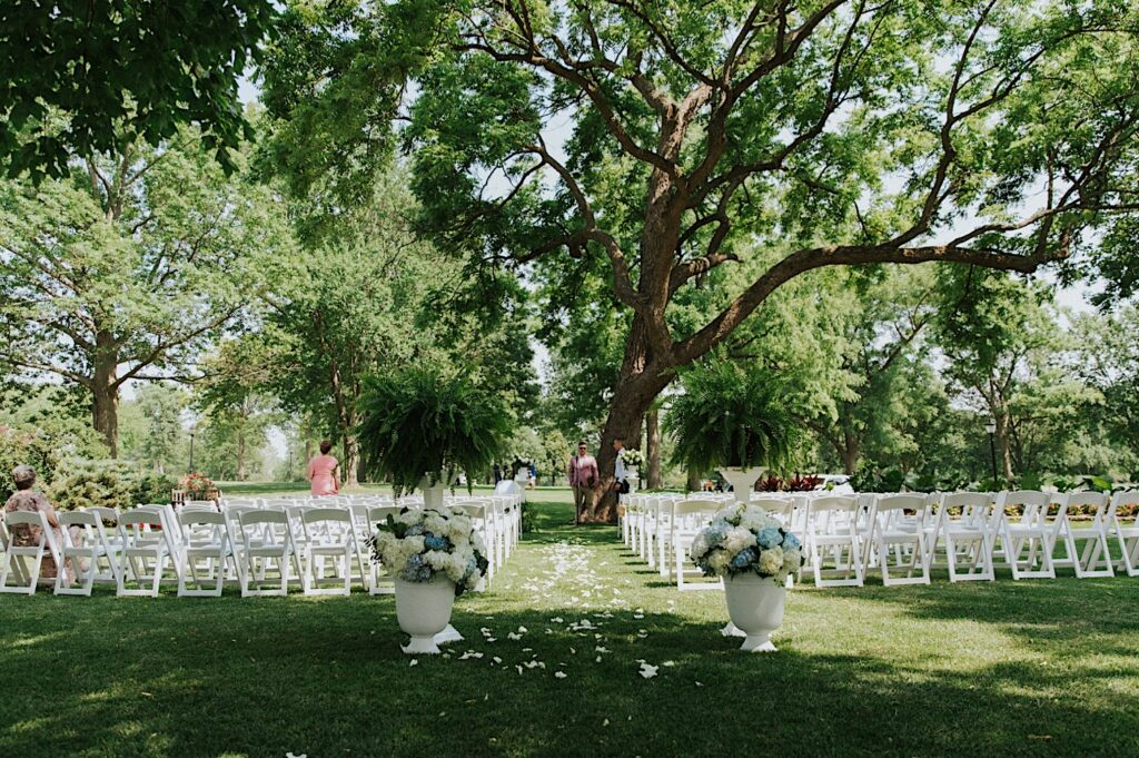 A backyard in Springfield Illinois is decorated for a wedding ceremony with  white chairs, floral decorations, and flower petals on the aisle