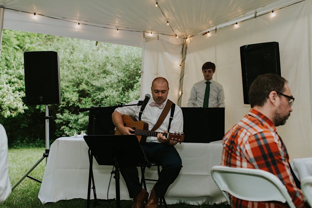 A man sits and plays an acoustic guitar during a backyard wedding in Springfield Illinois, he is one of the vendors of the wedding
