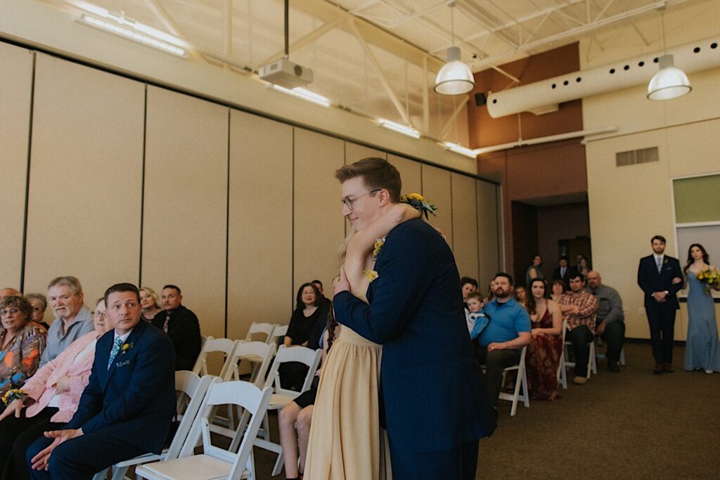 A groom hugs his mom after walking down the aisle of his indoor wedding ceremony at Erin's Pavilion