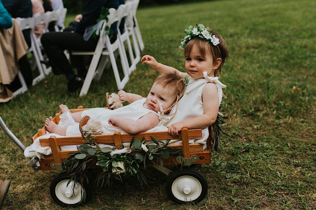 During a backyard wedding in Springfield Illinois two small children ride in a small wooden cart as flower girls