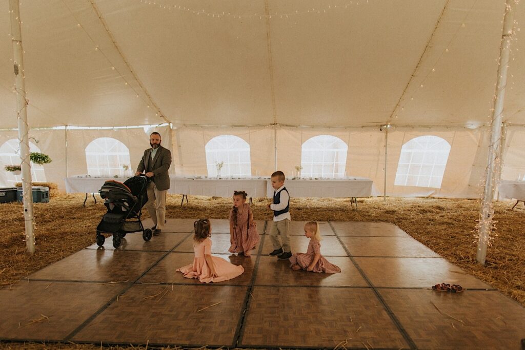 4 children and a father stand on a dancefloor set up underneath a tent for a backyard wedding in Springfield Illinois, the dancefloor is from one of the wedding vendors