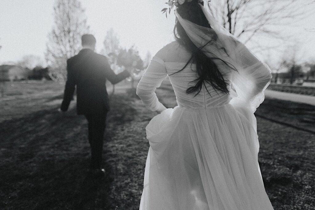 Black and white photo of a bride walking away from the camera towards the groom who is also walking away towards a field outside Erin's Pavilion