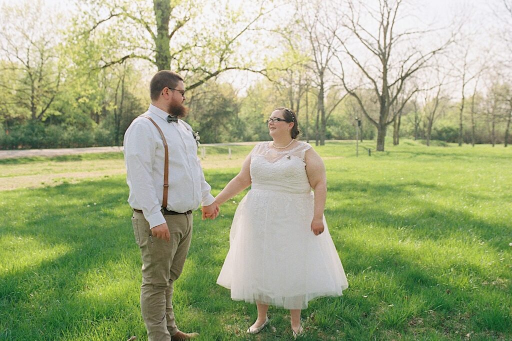 Film photo of a bride and groom looking at one another while standing in a field and holding hands