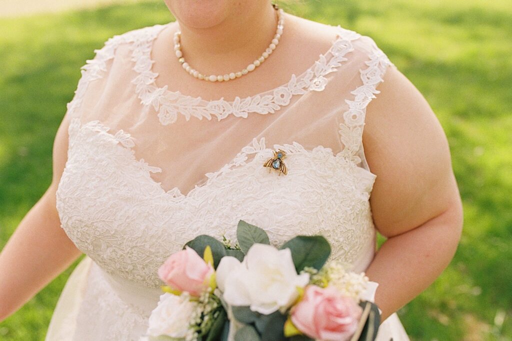 Close up photo of a bride in her wedding dress, on her chest is a jewel pendant of a bug