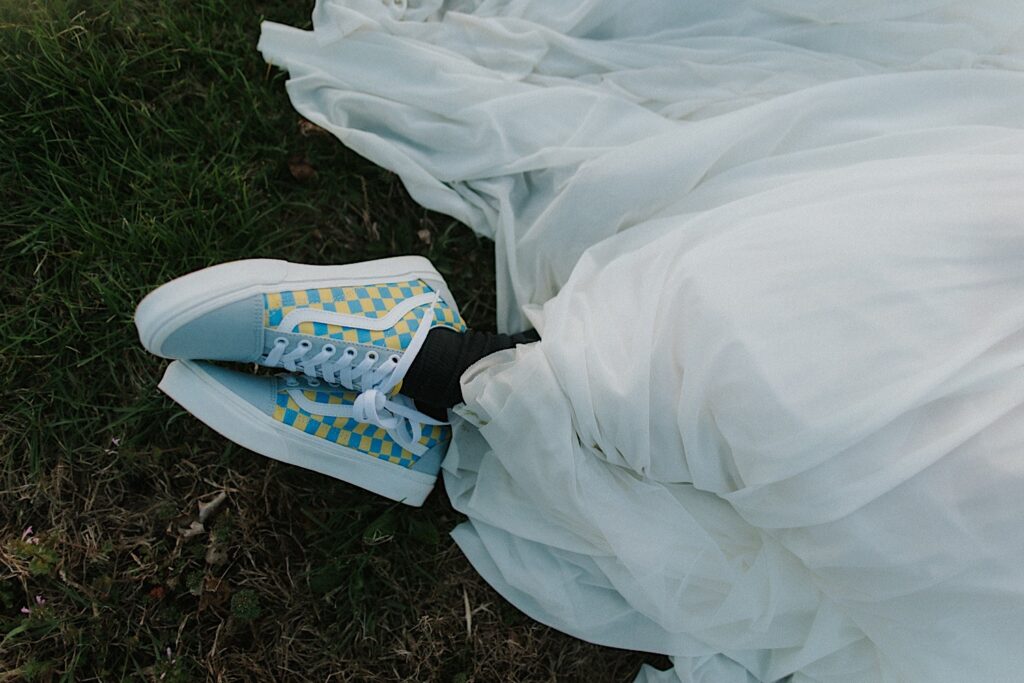Knee down photo of a bride laying in the grass with her custom Vans shoes on her feet