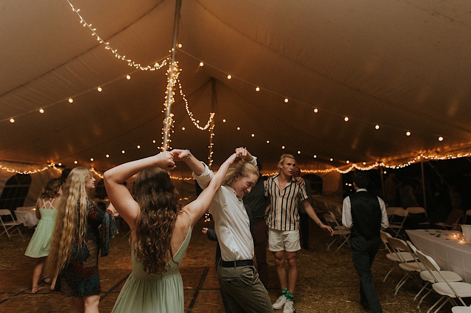 Guests of a backyard wedding in Springfield Illinois dance together under a tent with string lights