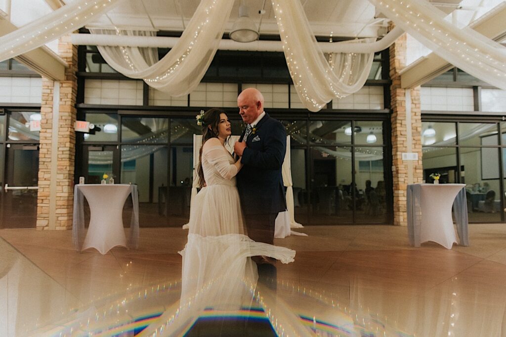A bride dances with her father during her wedding reception at Erin's Pavilion, the reception space is decorated with large fabric pieces across the ceiling with string lights in them