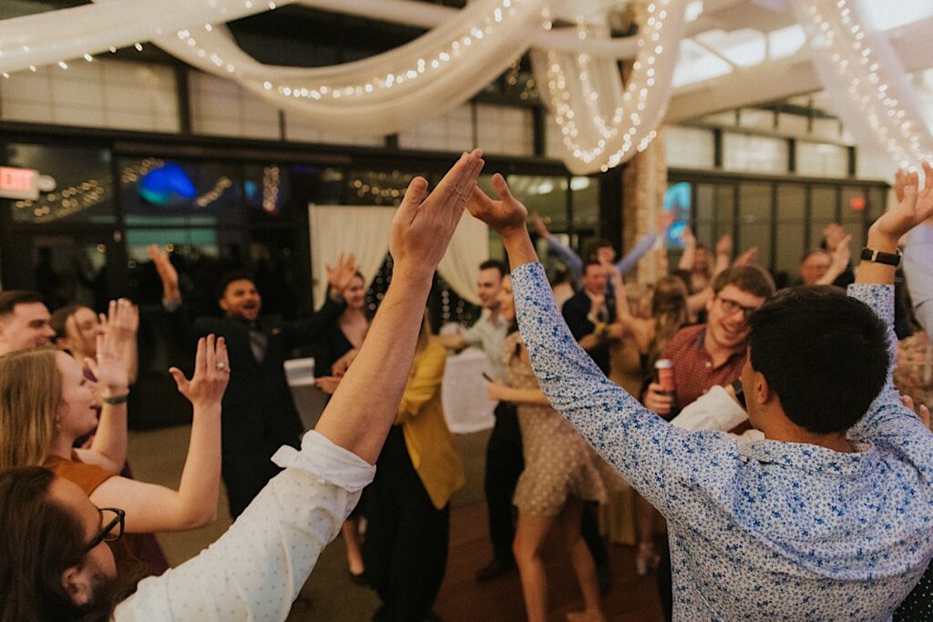 Guests of a wedding reception at Erin's Pavilion lift their hands up during the YMCA