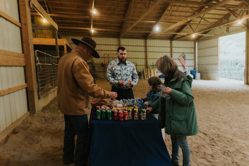 In a barn in Springfield Illinois a groom helps his family set up a table with snacks and drinks before their backyard wedding ceremony