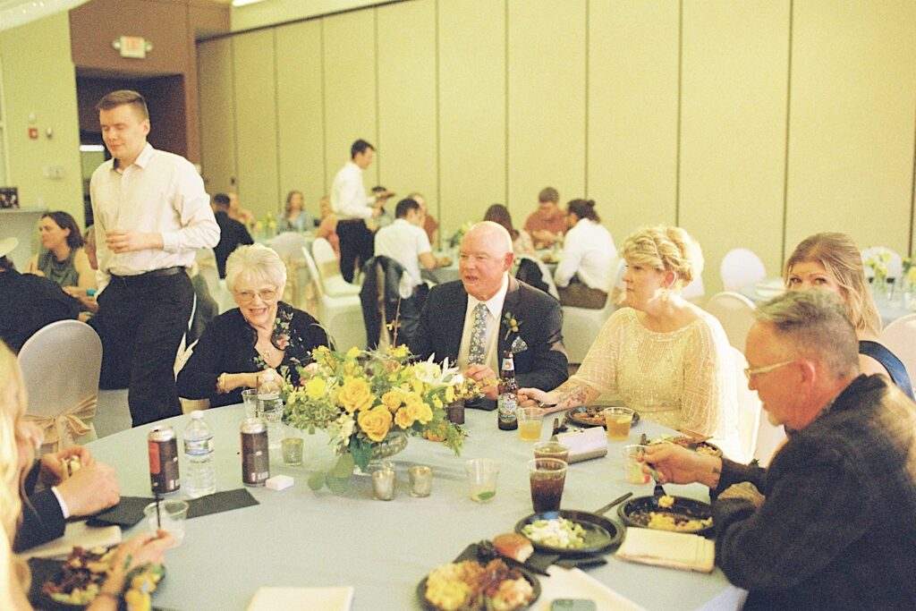 Film photo of guests of a wedding seated at a table talking with each other