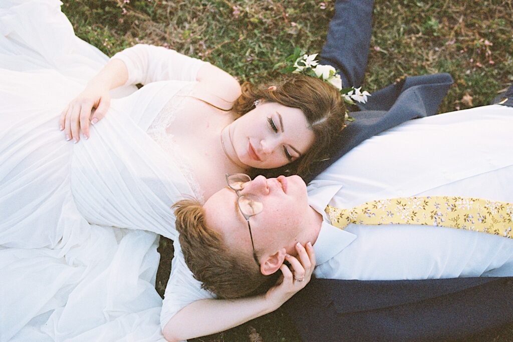 Film photo of a bride and groom laying in the grass and looking at one another taken by a documentary wedding photographer