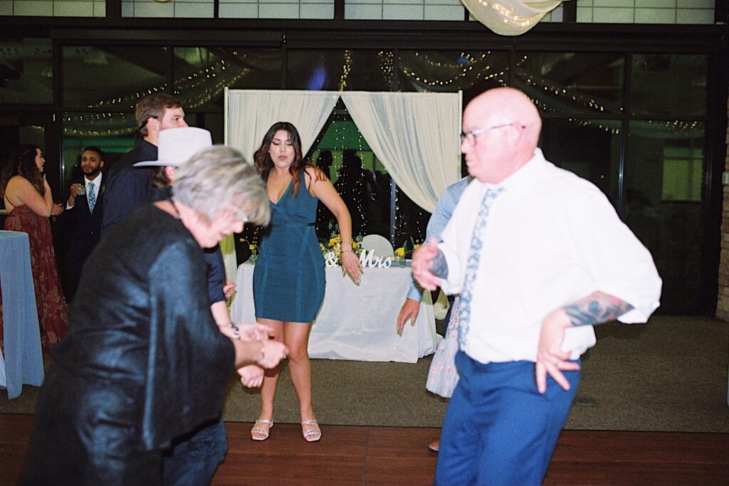 Film photo of guests of an indoor wedding reception on the dancefloor all dancing together