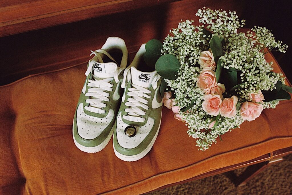 A photo of a wedding ring sitting on a pair of Nike Air's next to a bouquet on a bench