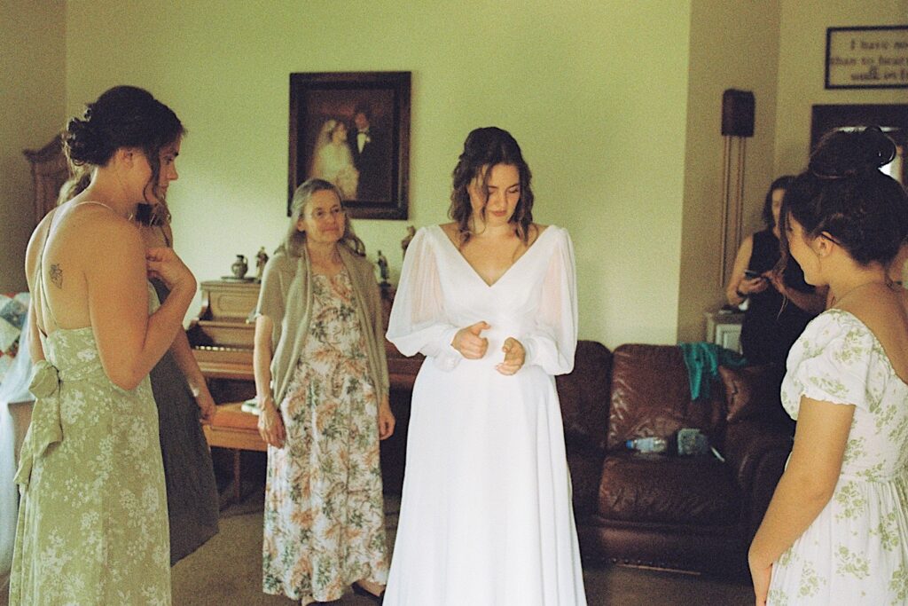 Film photo of a bride in her wedding dress standing in a room surrounded by her bridesmaids after getting ready for her wedding, taken by a documentary wedding photographer