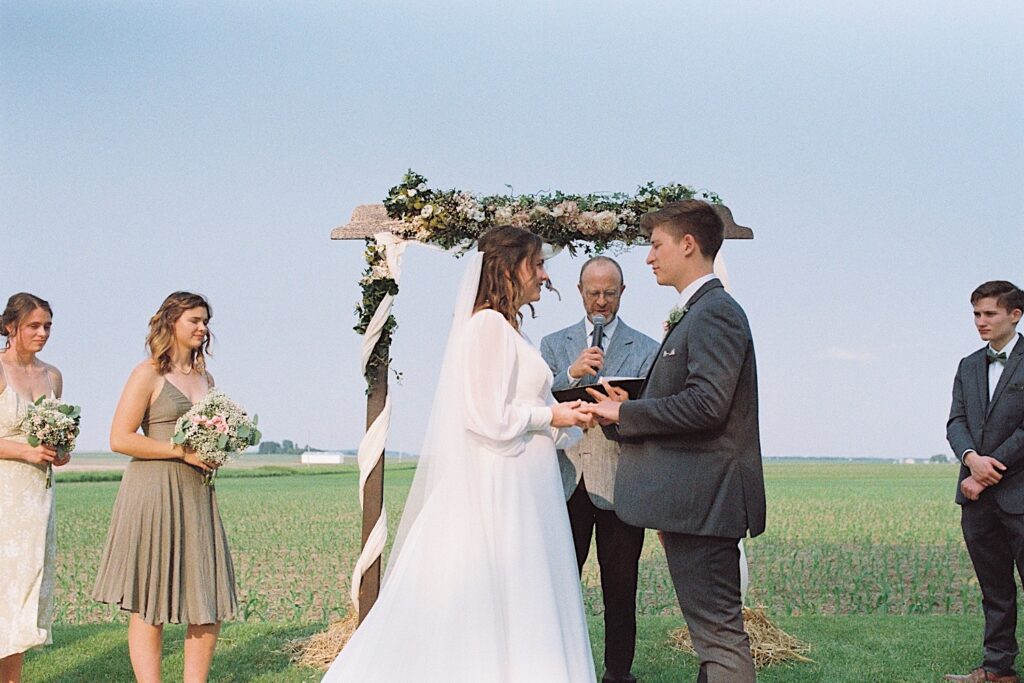 Film photo of a bride and groom during their wedding ceremony in a field as their officiant speaks, taken by a documentary wedding photographer