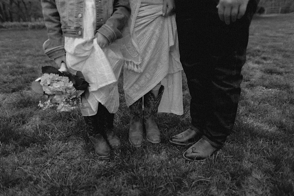 Black and white photo of a bride and groom and their daughter all showing off their cowboy boots in their backyard before their wedding day in Springfield Illinois
