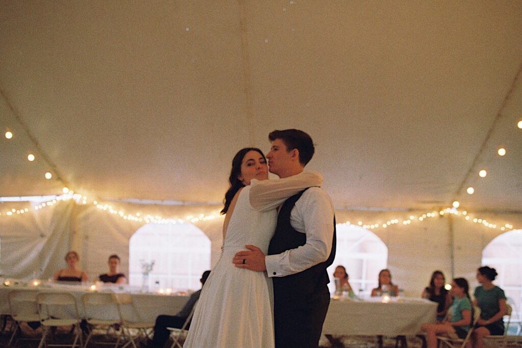 Film photo of a bride and groom dancing underneath a tent during their wedding reception, taken by a documentary wedding photographer