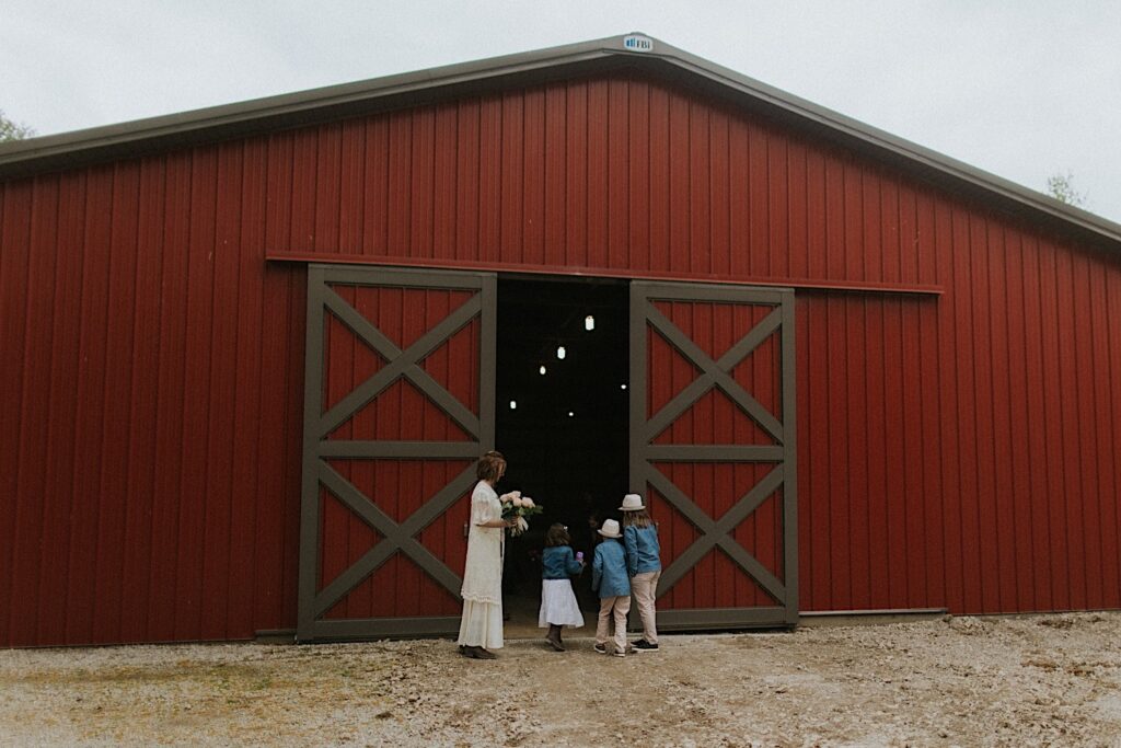 A bride stands with 3 children at the entrance of a barn as they get ready to head in to celebrate their backyard wedding ceremony in Springfield Illinois