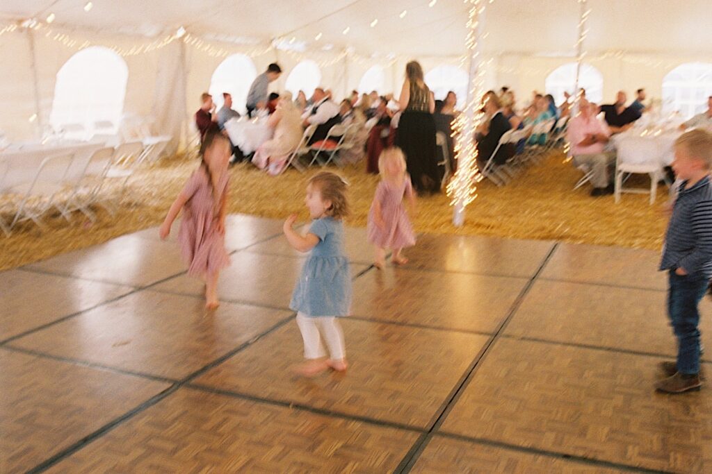 Blurry film photo of 4 children dancing on a dance floor in a tent at a wedding reception, taken by a documentary wedding photographer