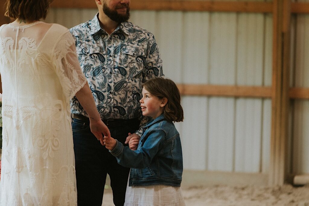 A daughter holds her mother and father's hands as they stand in a barn in their backyard before their wedding ceremony in Springfield Illinois