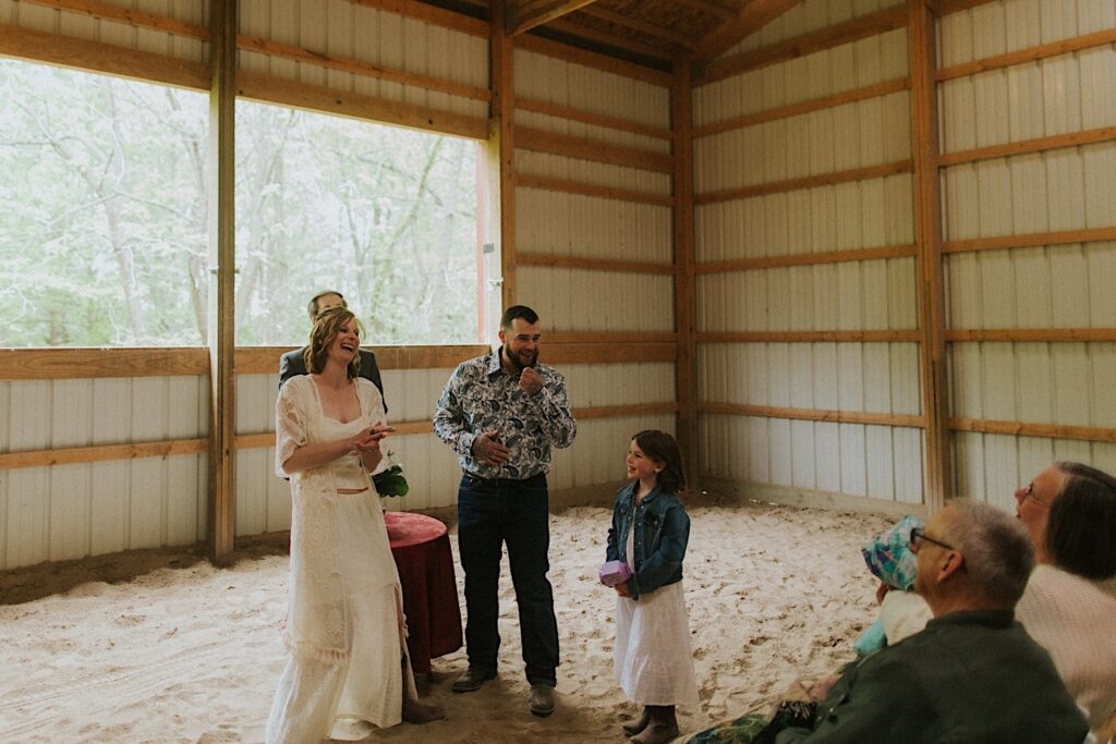 A bride and groom and their daughter smile and laugh after their ceremony inside their barn in the backyard of their Springfield Home
