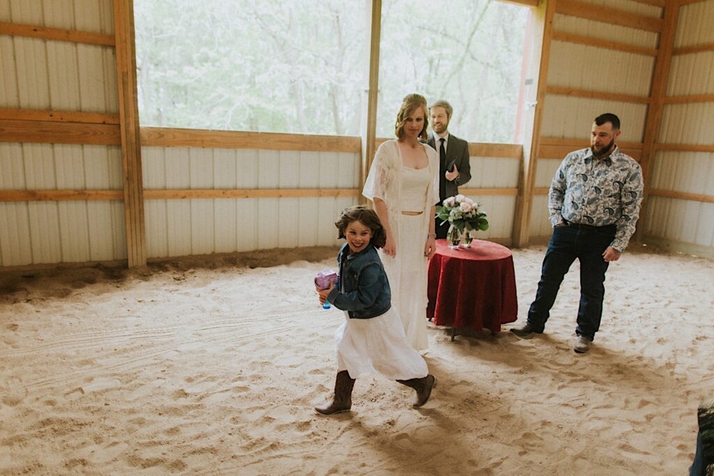A child with a bubble gun runs and smiles in a barn as her parents look on, they just had their wedding ceremony in the barn which is in the backyard of their Springfield home