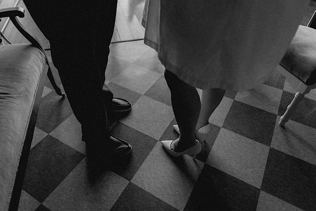 Black and white photo of a couple waist down standing on a tile floor