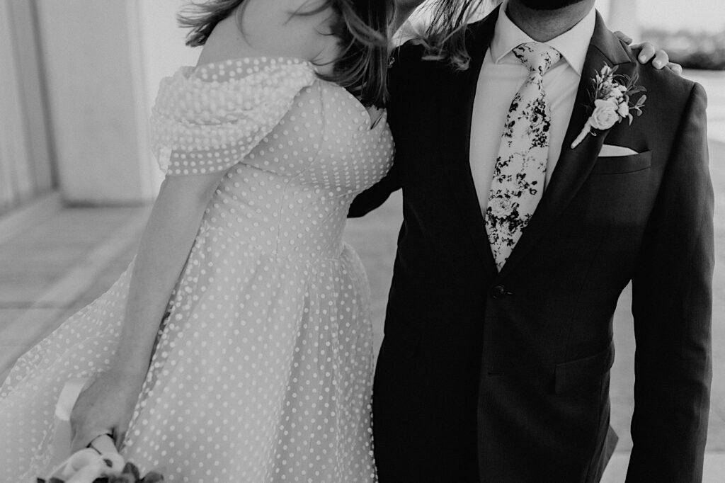 Black and white photo of a bride and groom from their shoulders down showing of their wedding attire