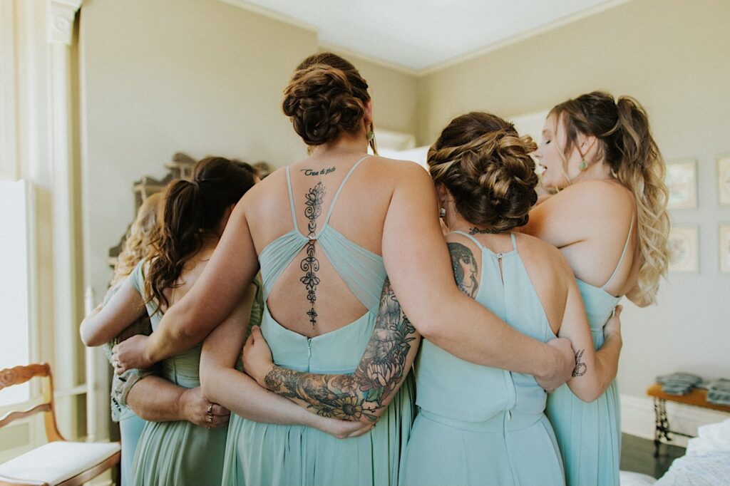 A group of bridesmaids all huddle up with their arms around one another after getting ready for a wedding