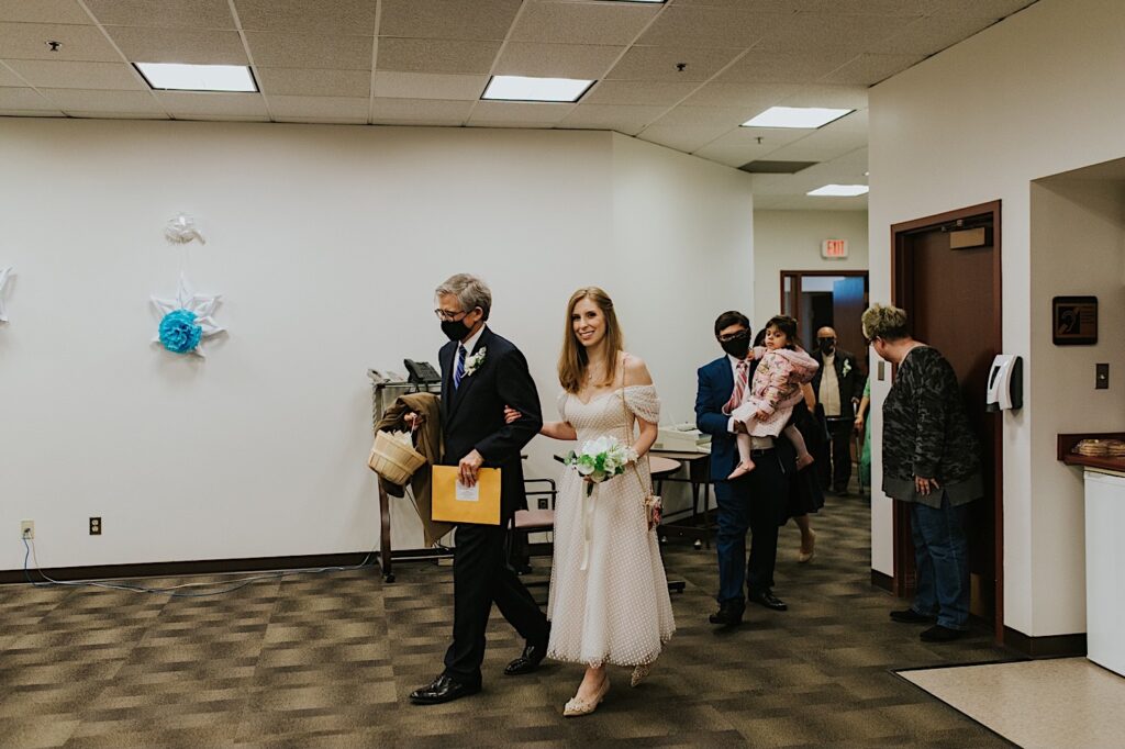 During their elopement at the Sangamon County Courthouse a bride is walked in by her father towards the groom