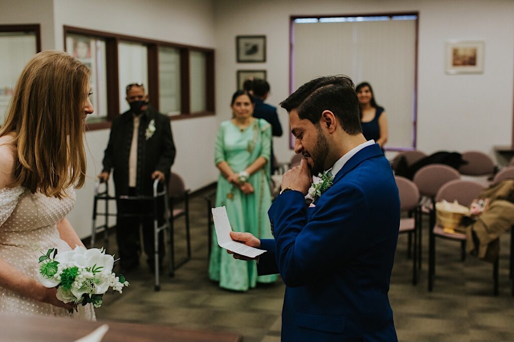 During their elopement at the Sangamon County Courthouse a groom reads his vows to the bride as she smiles at him with their families watching behind them