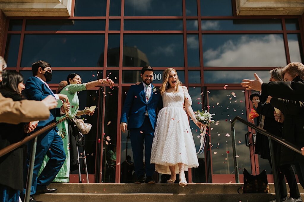 A bride and groom walk together and smile while exiting the Sangamon County Courthouse as their families on either side throw flower petals in the air