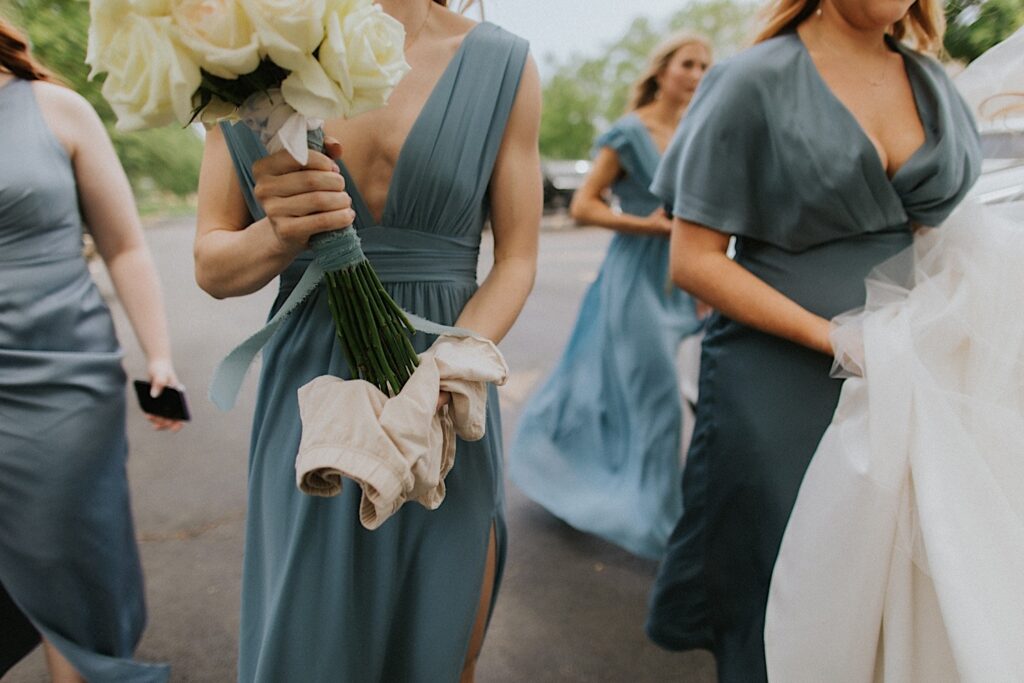Shoulder down photo of bridesmaids walking in the street with one of them holding a bouquet of flowers with a towel on their stems