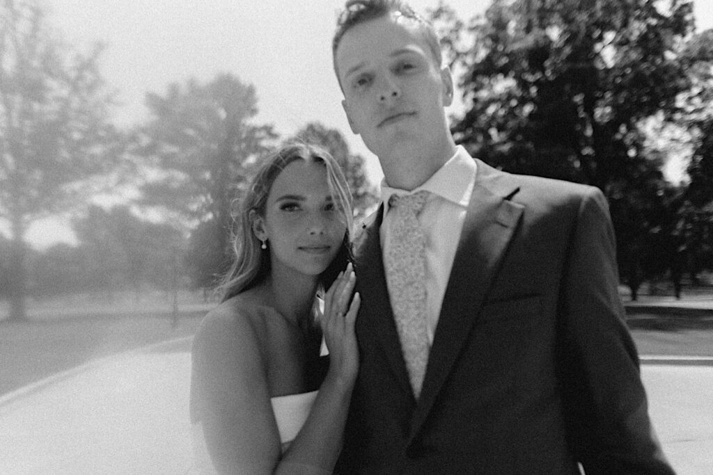 Black and white film photo of a bride and groom standing next to one another and looking at the camera before their wedding ceremony at Bloomington Country Club
