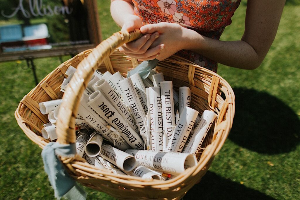 A woman holds a wicker basket filled with rolled up fake newspapers with headlines about the wedding
