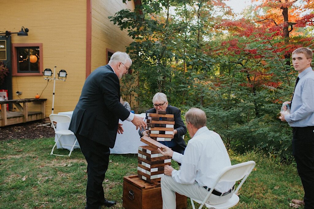 A group of 4 men sit around a tower of giant jenga blocks in a backyard and play the game together