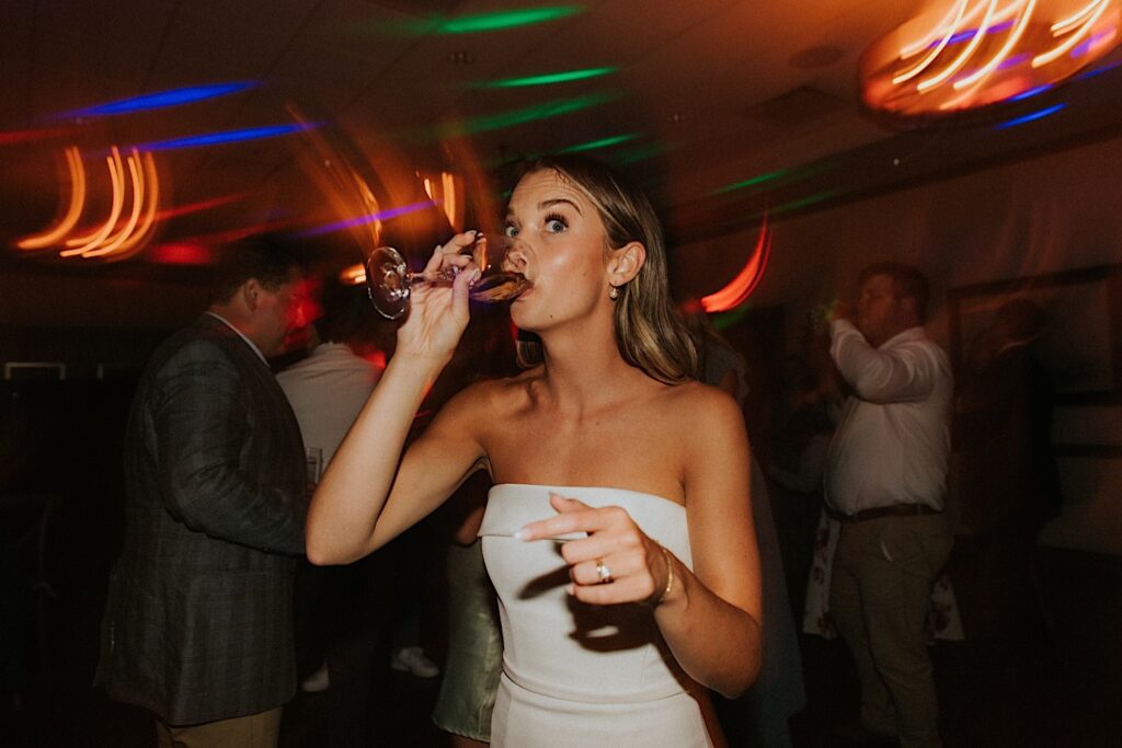 A bride drinks from a glass while on the dance floor of her indoor wedding reception at Bloomington Country Club