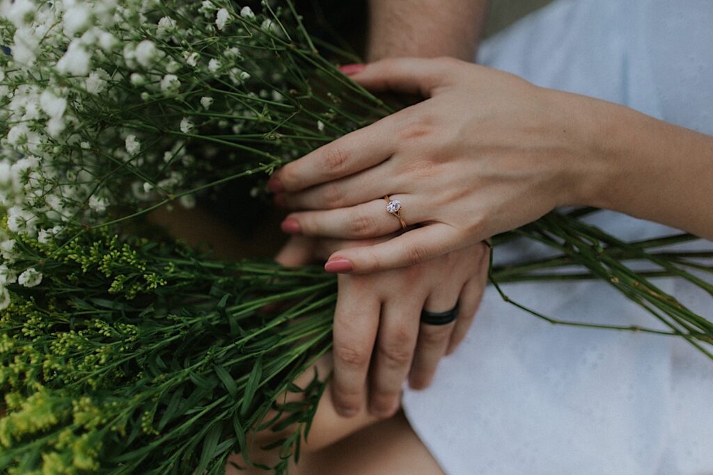Close up photo of a man and woman's hands, each with an engagement ring on them, laying on top of one another while holding flower bouquets during their engagement session at Allerton Park