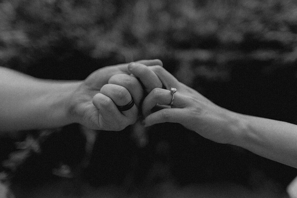 Black and white photo of a man and a woman's hand, each with an engagement ring on it, reaching out and holding one another during their engagement session at Allerton Park