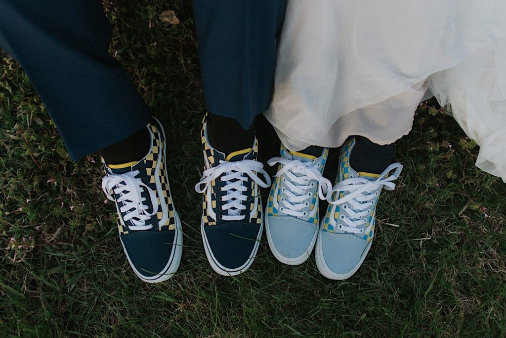 Close up top down photo of a couple's Vans shoes that they are wearing on their wedding day, the bride's dress and groom's pants are visible