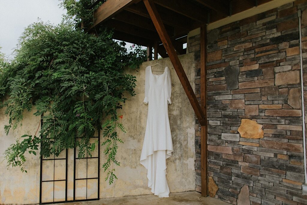 A wedding dress hangs in front of an outdoor stone wall