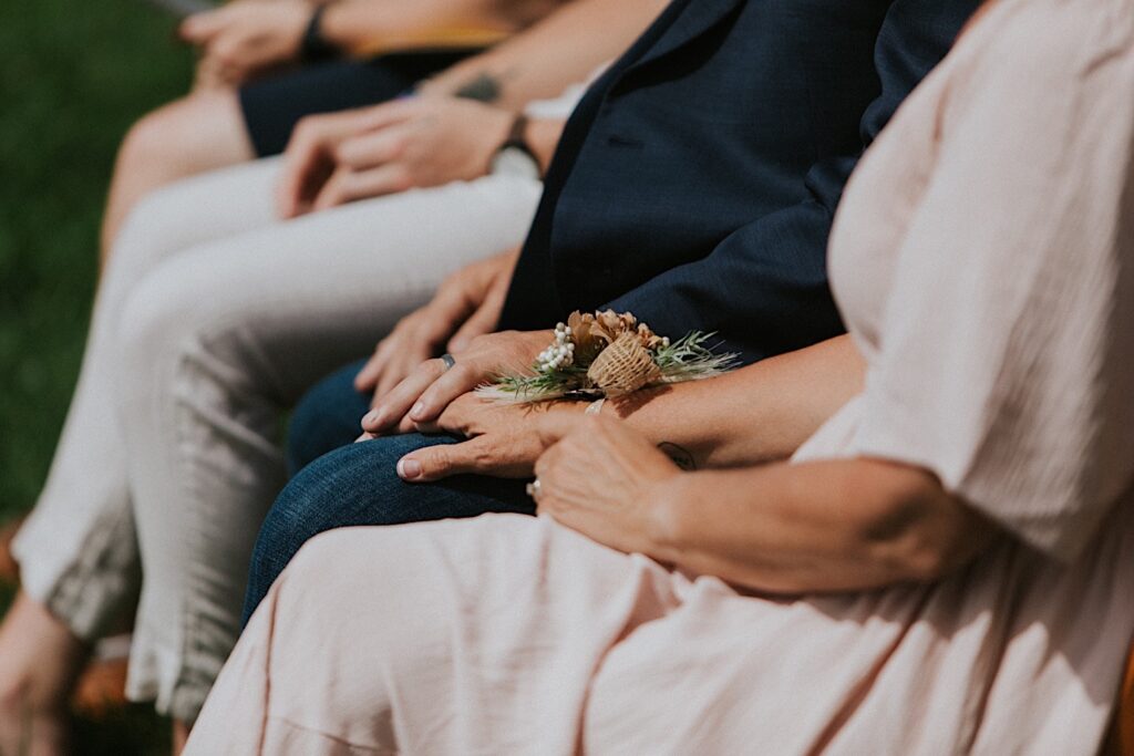 Close up photo of guests of a wedding that are seated holding hands during the ceremony