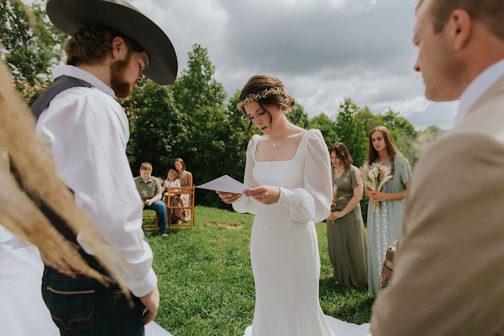 A bride reads her vows during the ceremony of her intimate destination wedding in Tennessee, the groom stands across from her while guests around them watch