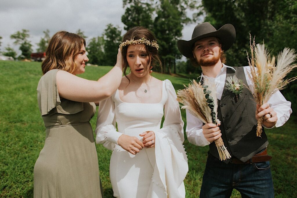 A groom smiles at the camera as the bride next to him has a woman help adjust her hair while they stand outside after the ceremony of their intimate destination wedding in Tennessee