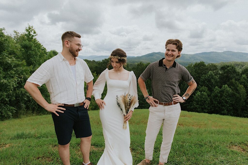 A bride stands and poses with two guests of her wedding, behind them are mountains in the distance
