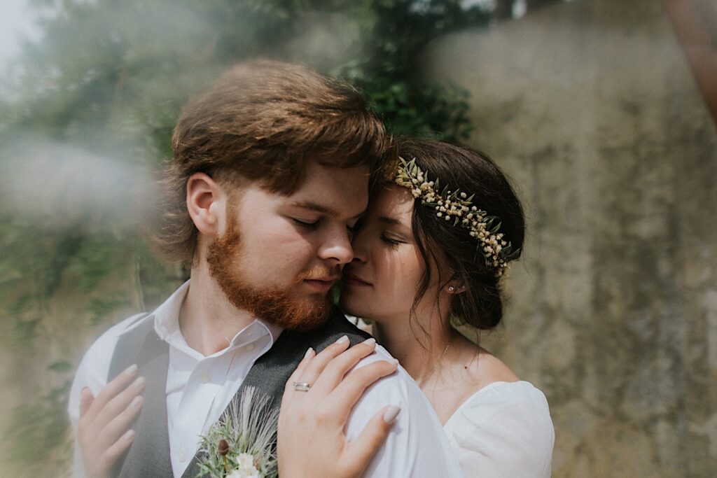 During portraits of their intimate destination wedding in Tennessee, a bride hugs the groom from behind and is about to kiss him on the cheek 